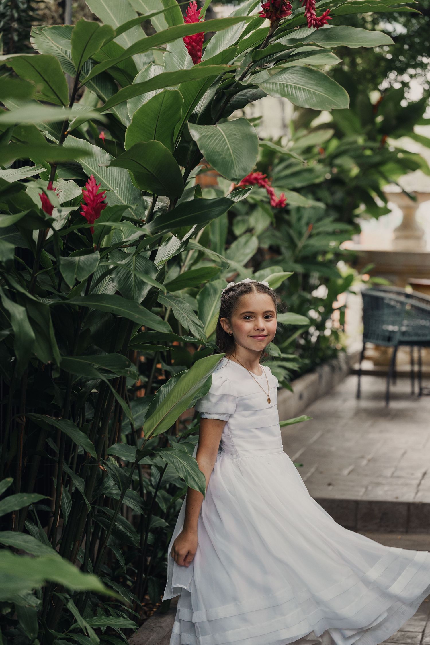 White dress twirling against lush tropical garden backdrop with red flowers.