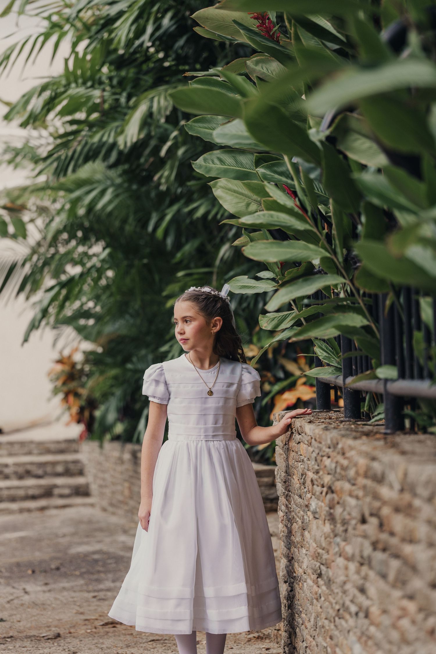 White dress flowing in garden setting with stone wall and tropical plants.