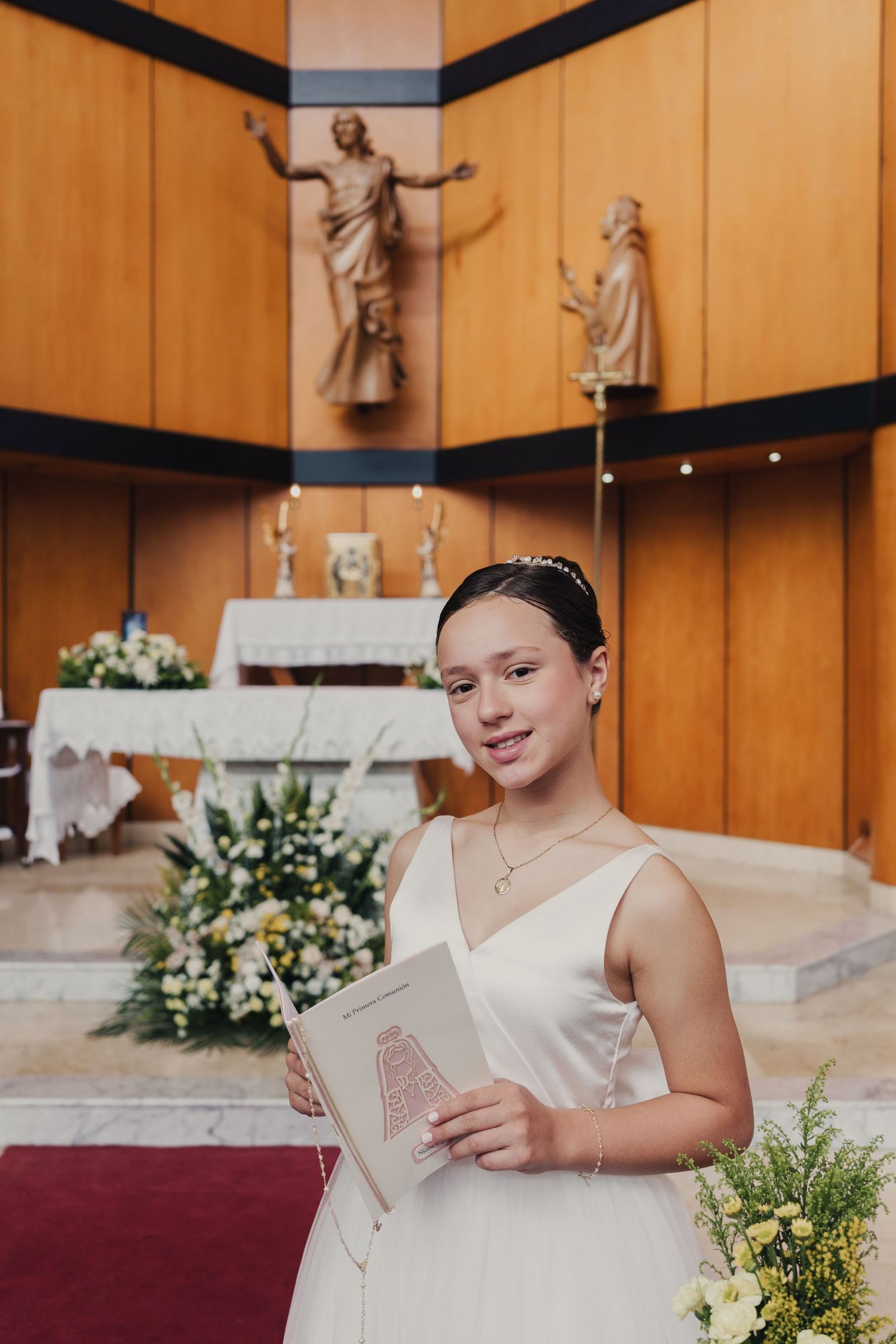 A young attendant in a white dress sits in a church pew reading a program during a wedding ceremony.
