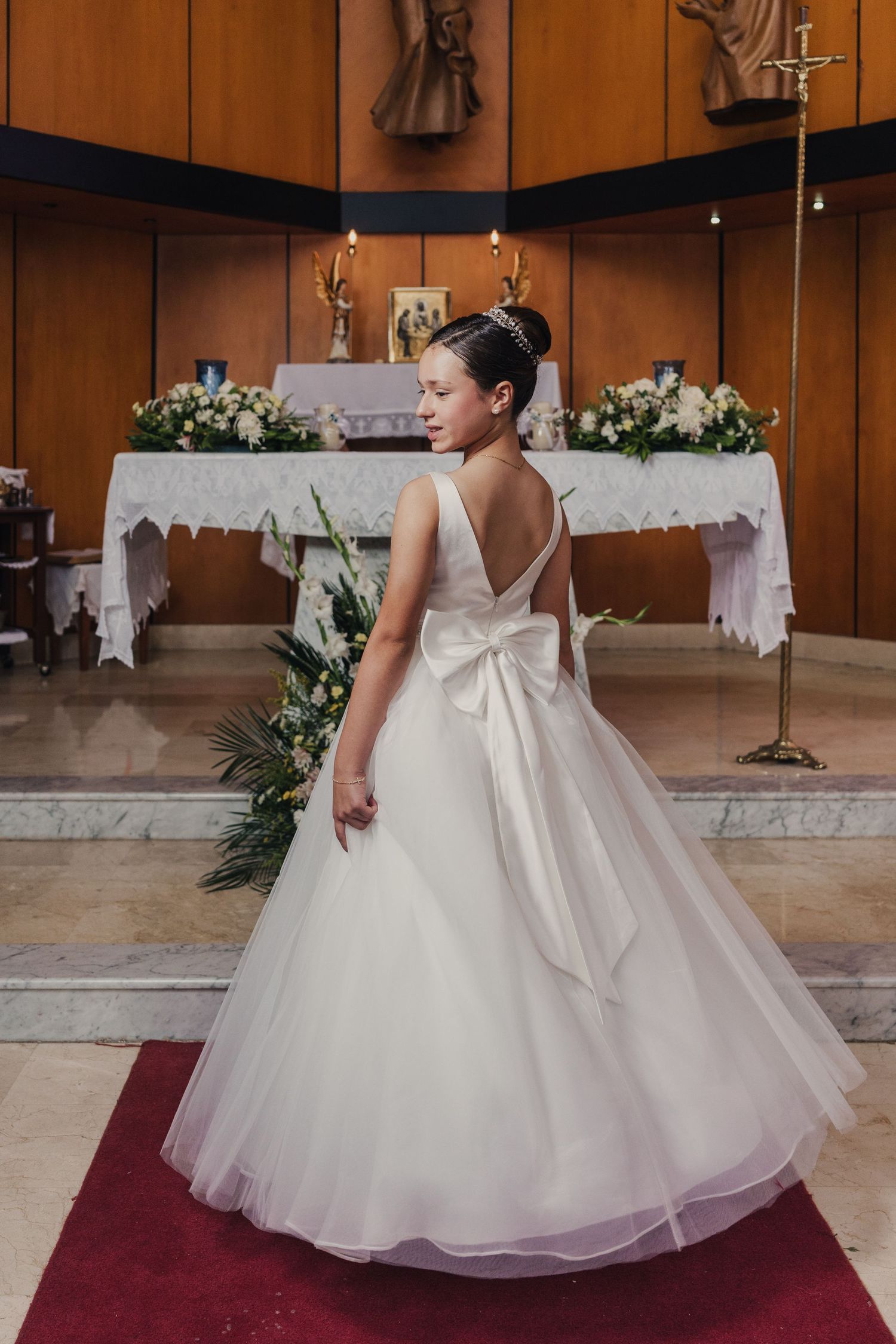 A bride in a voluminous white ballgown with tulle skirt twirls gracefully on a red carpet in a wood-paneled room.