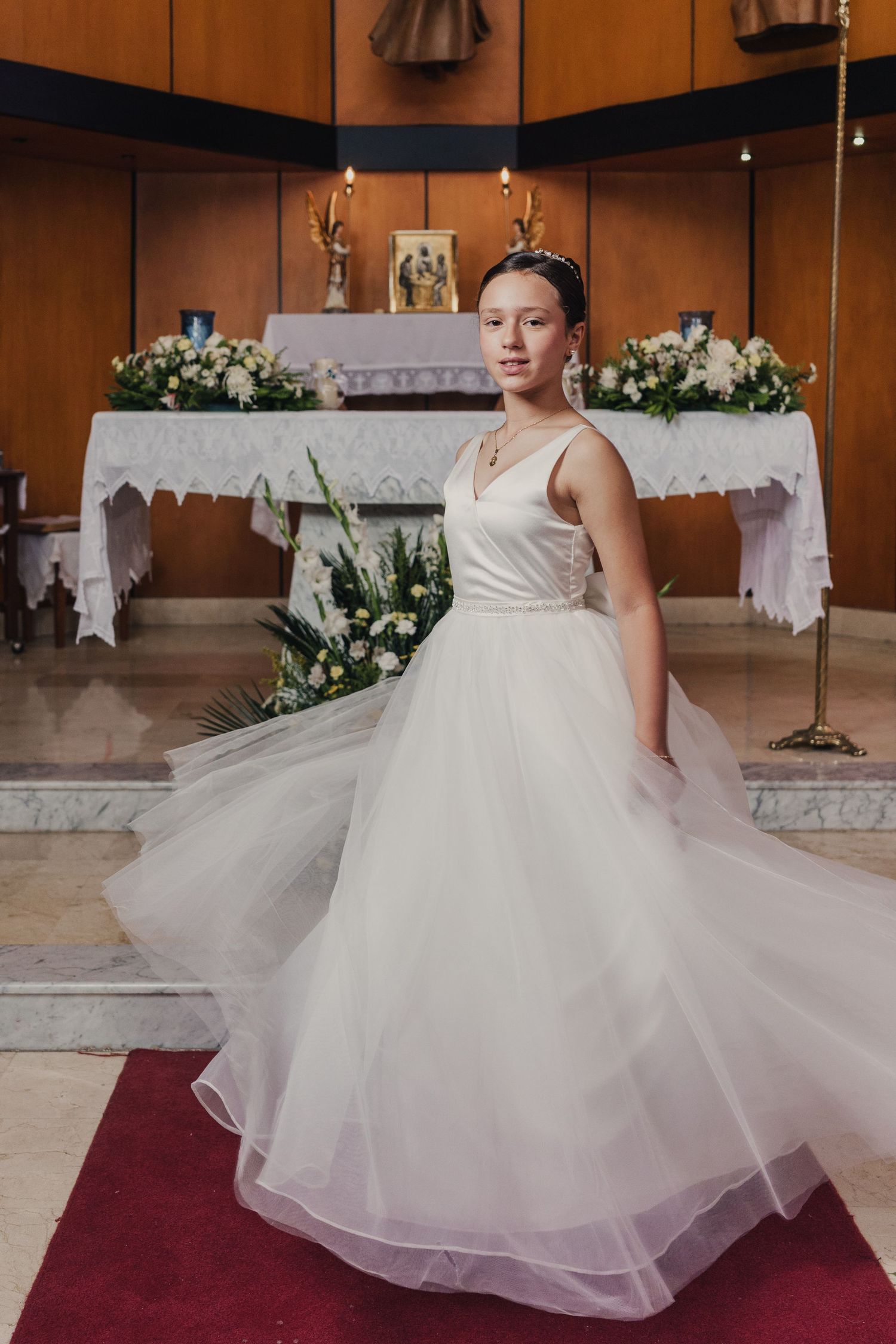 A bride in a flowing white ballgown poses in a church with floral arrangements and candles in the background.