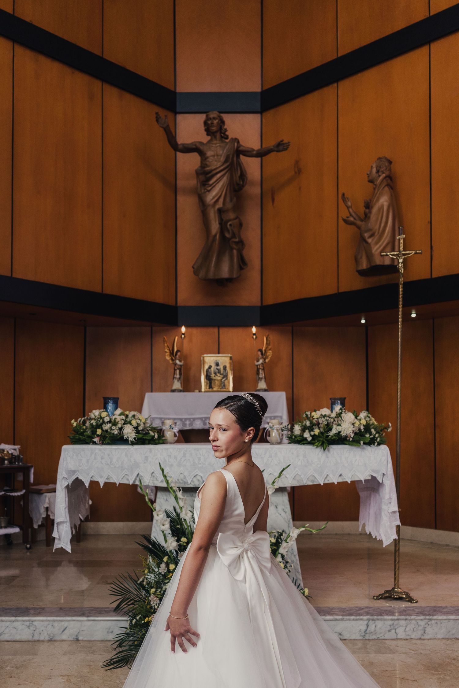 A ballet dancer performs graceful movements in front of a church altar decorated with white flowers and linens.