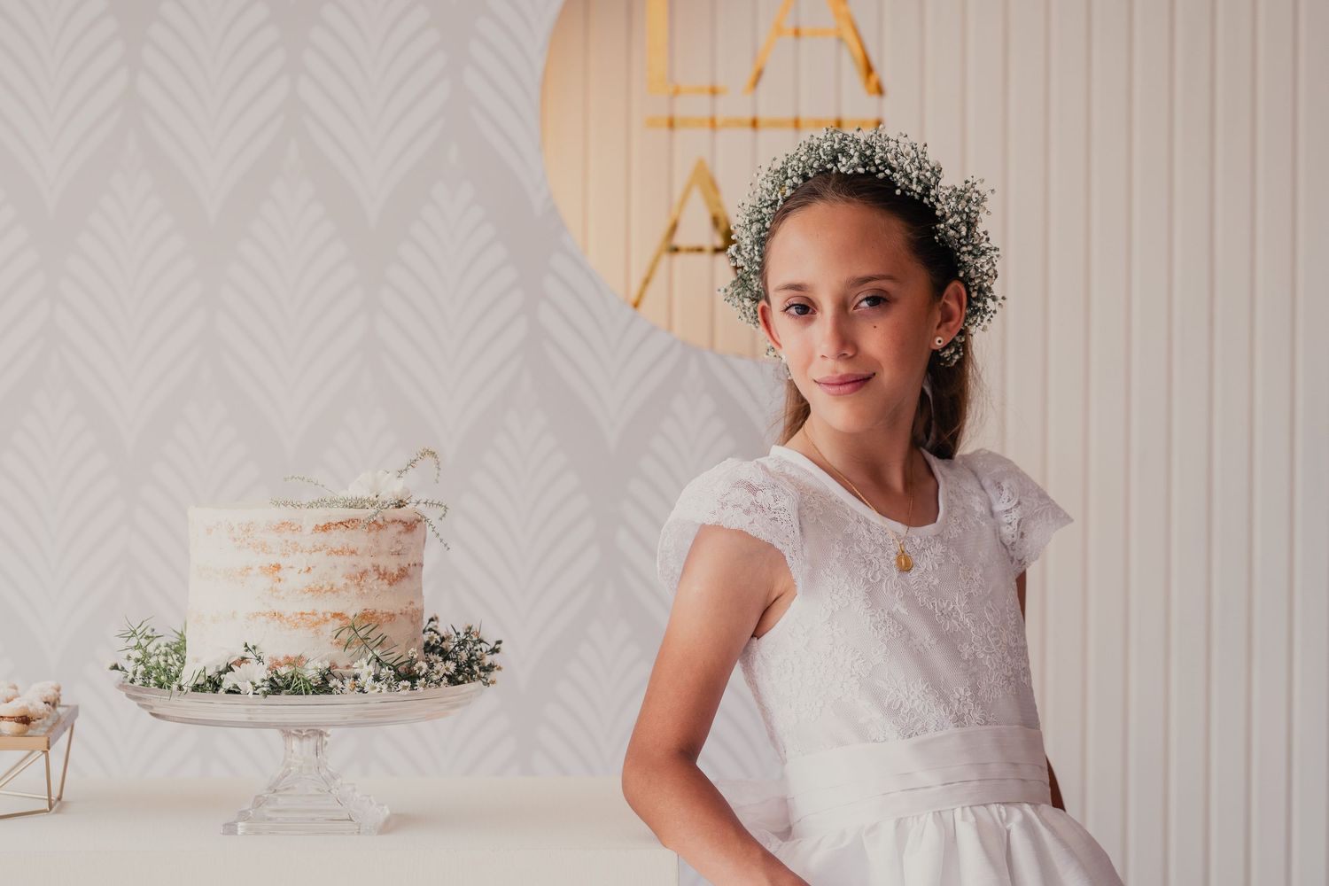 Young girl in a white lace dress and floral crown poses during a special occasion celebration.