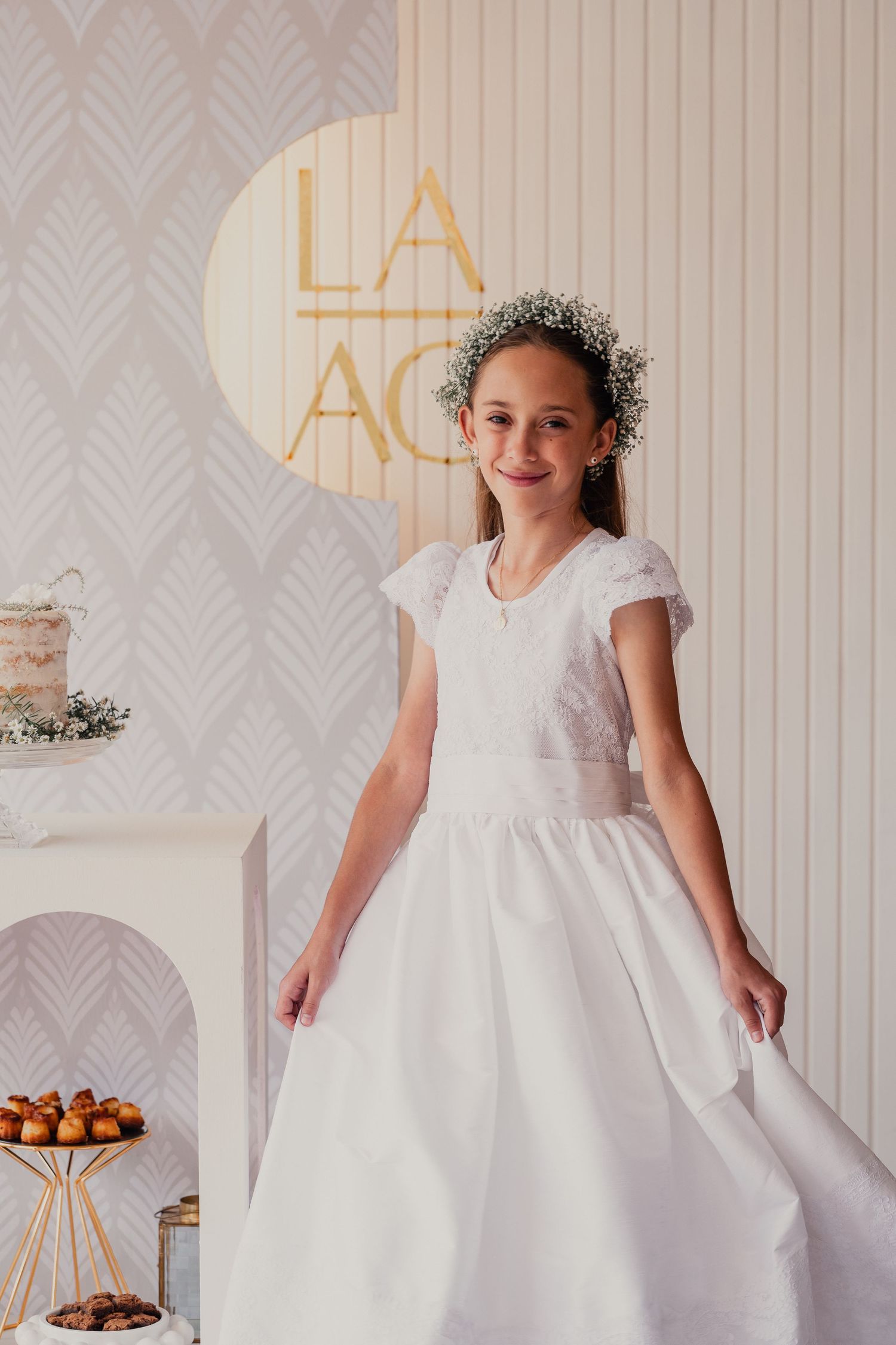A young person wearing a white formal dress with cap sleeves twirls in front of a decorative wall with gold accents.