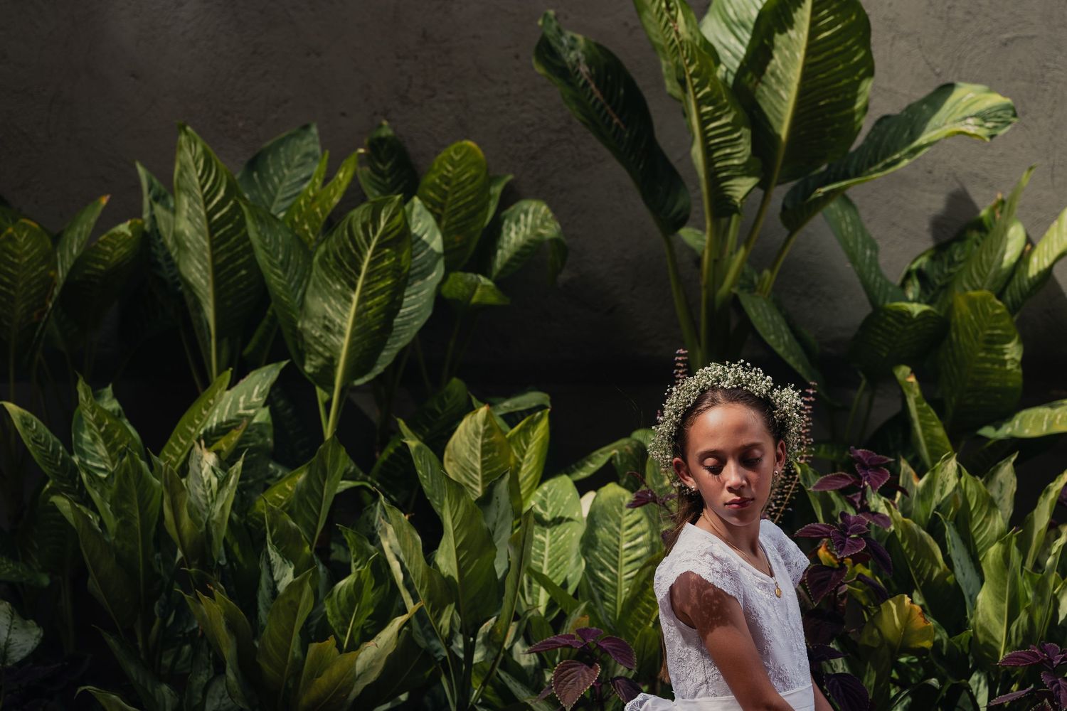Couple in wedding attire embraces while standing among lush green tropical plants in an outdoor garden setting.