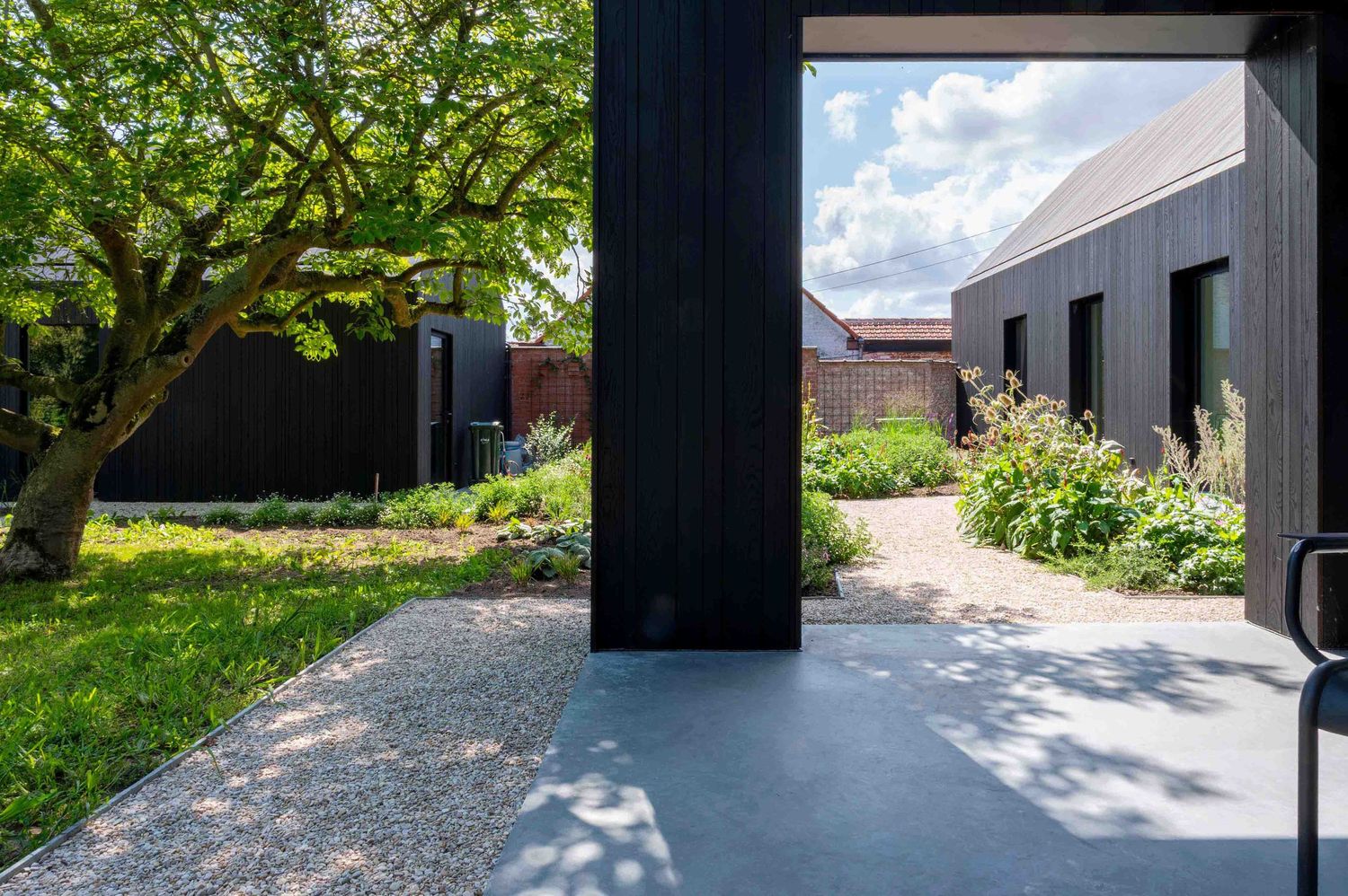 Moderne architectuur met zwarte zuilen en grindpaden, omringd door groen. Terras gelegd in polybeton.