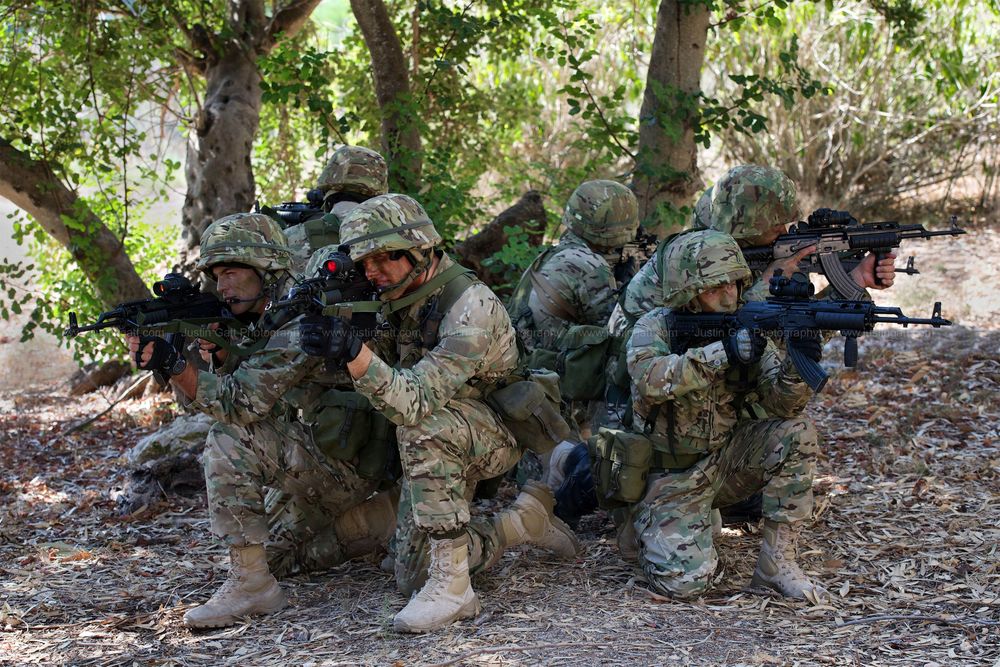 Military personnel in camouflage gear take defensive positions during a tactical training exercise.