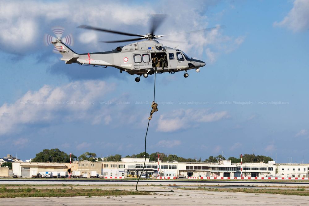 Military helicopter conducting low-altitude flight operations over coastal base.