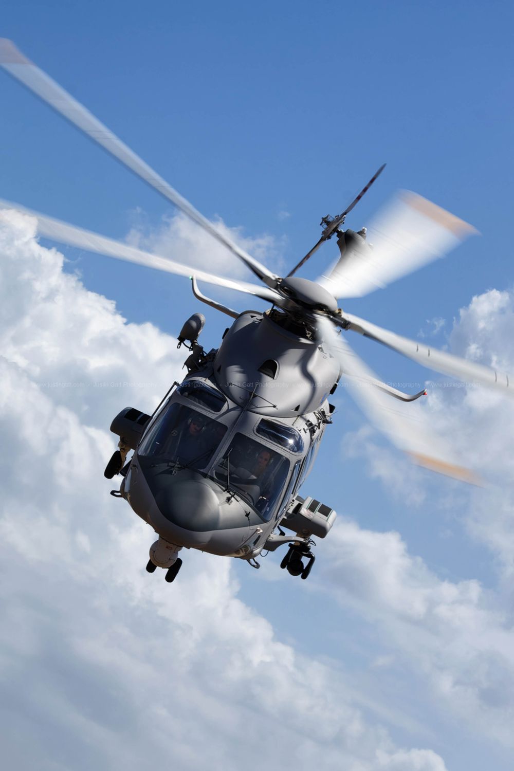 Military helicopter flying against blue sky with white clouds during daytime operations.