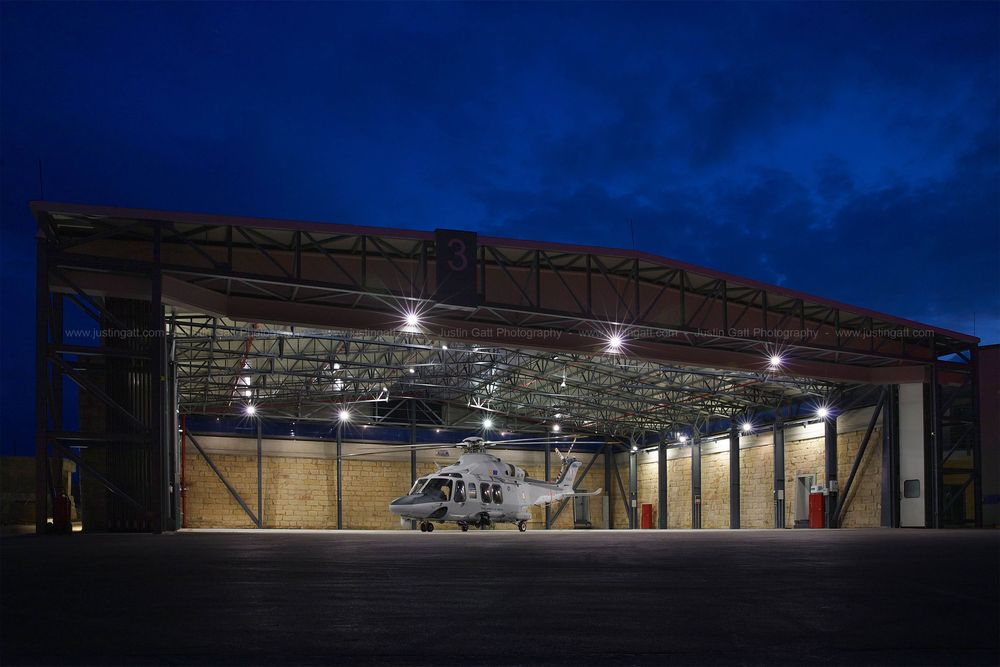 Aircraft hangar illuminated at dusk with large entrance doors visible.