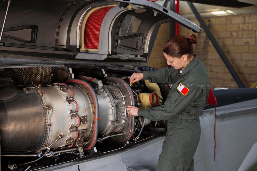 Military personnel inspecting and maintaining aircraft engine components in a hangar facility.