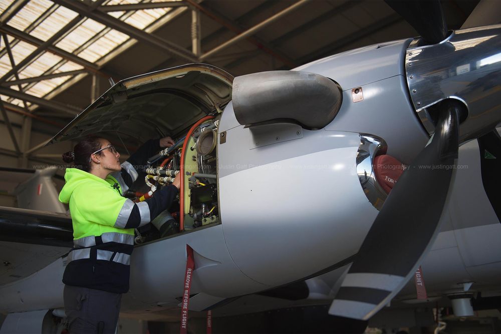 Aircraft maintenance technicians performing inspections under bright hangar lighting.