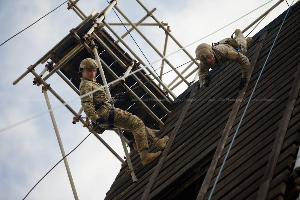 Military personnel conducting rope training exercises on an outdoor climbing structure.
