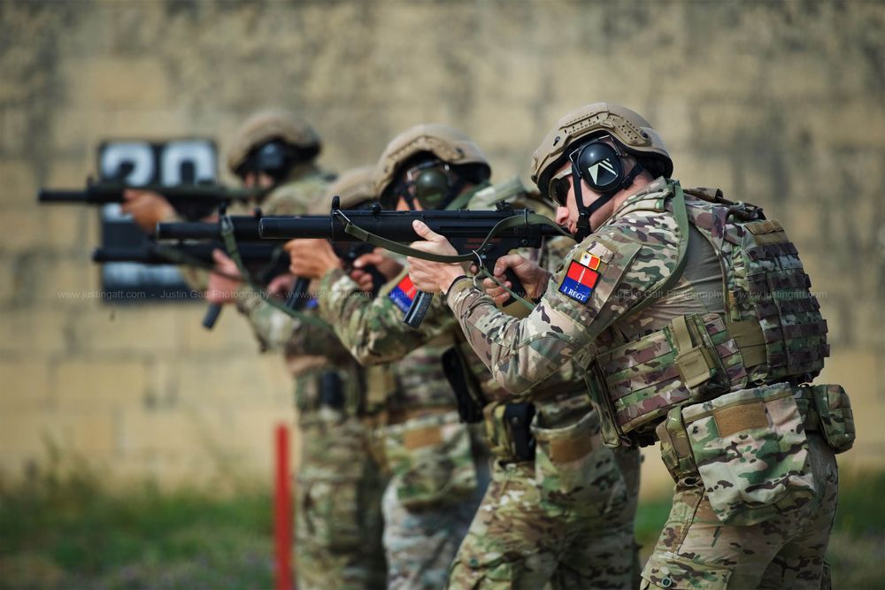 Military personnel in tactical formation with weapons during training exercise.