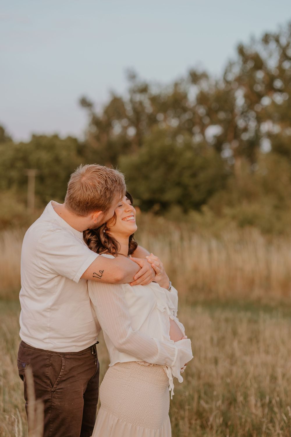 Sunset maternity photo of couple embracing in golden field.