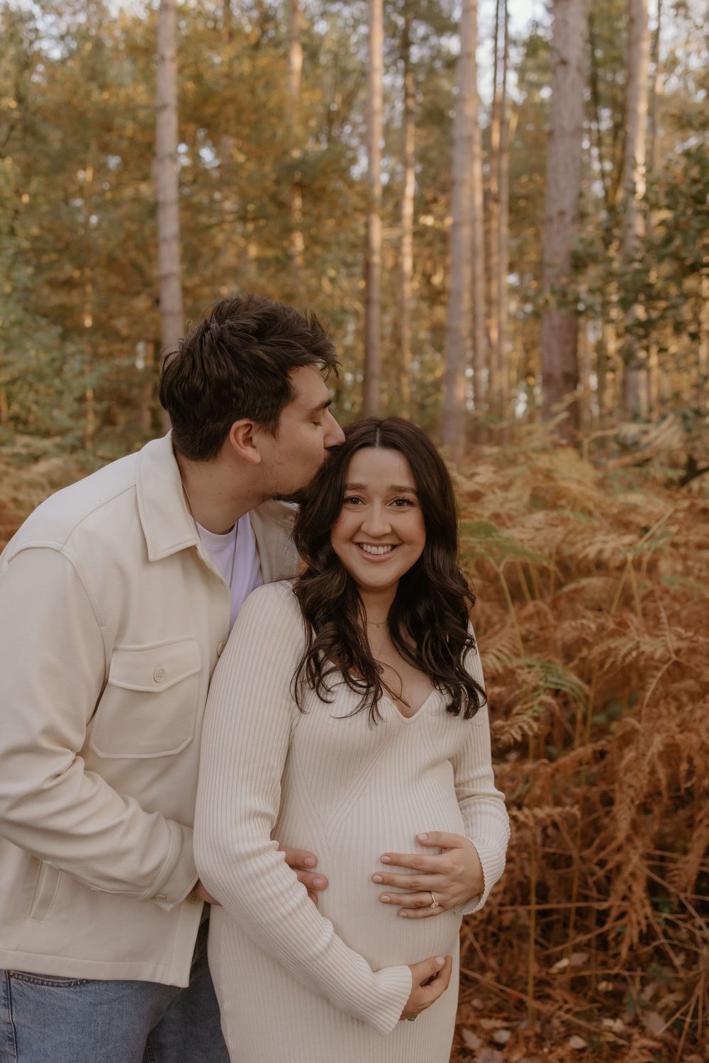 Expecting couple sharing intimate moments in an autumn forest with golden light.