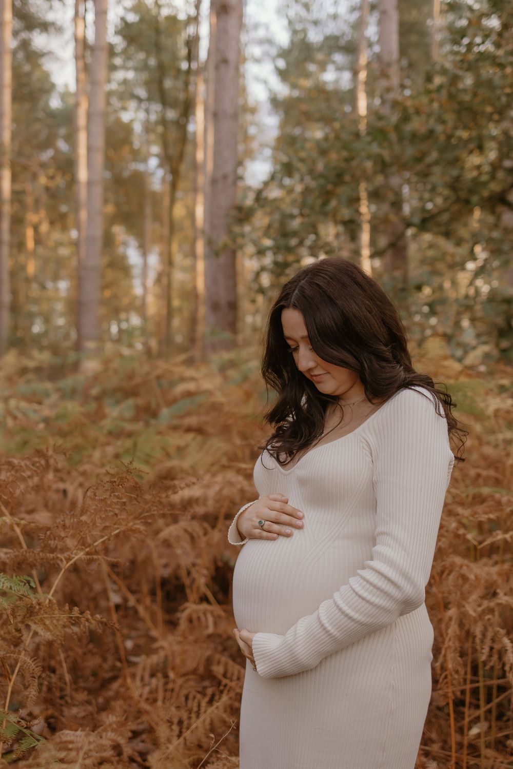 Maternity photos showing tender moments in a forest setting with warm autumn colors.