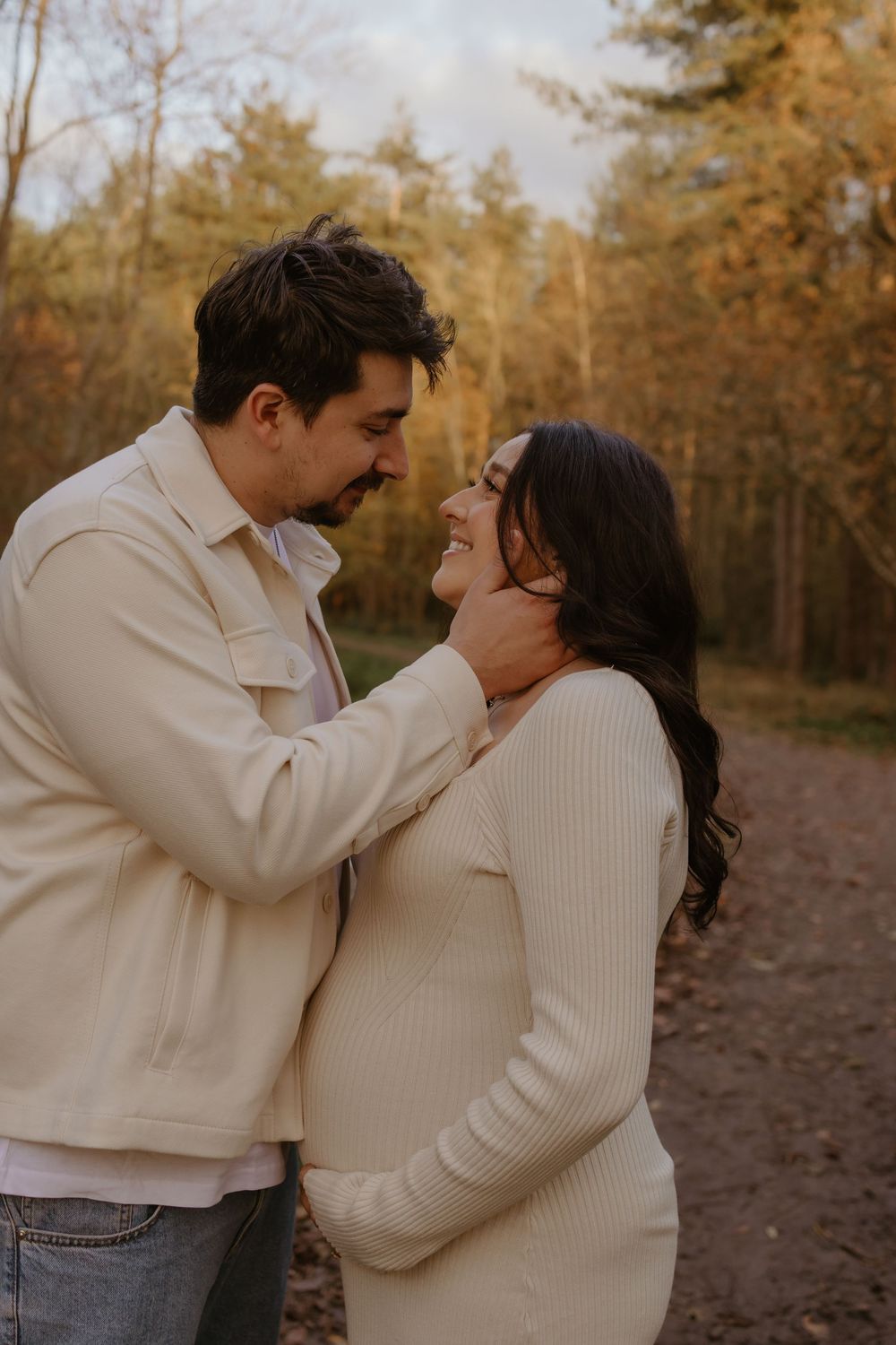 Romantic couple portraits in cream colored outfits against autumn forest backdrop.