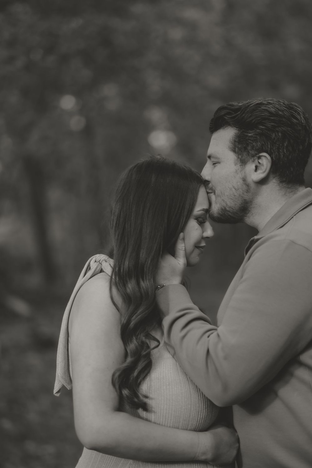 Romantic black and white portrait of an embracing couple in an intimate moment outdoors.