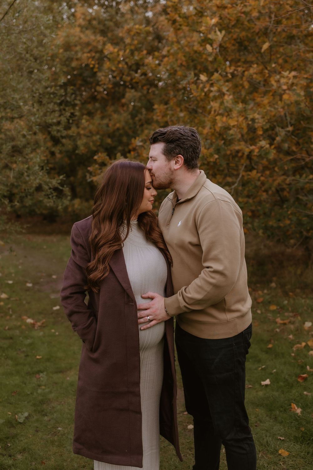 Tender moment between expecting couple against backdrop of fall foliage.