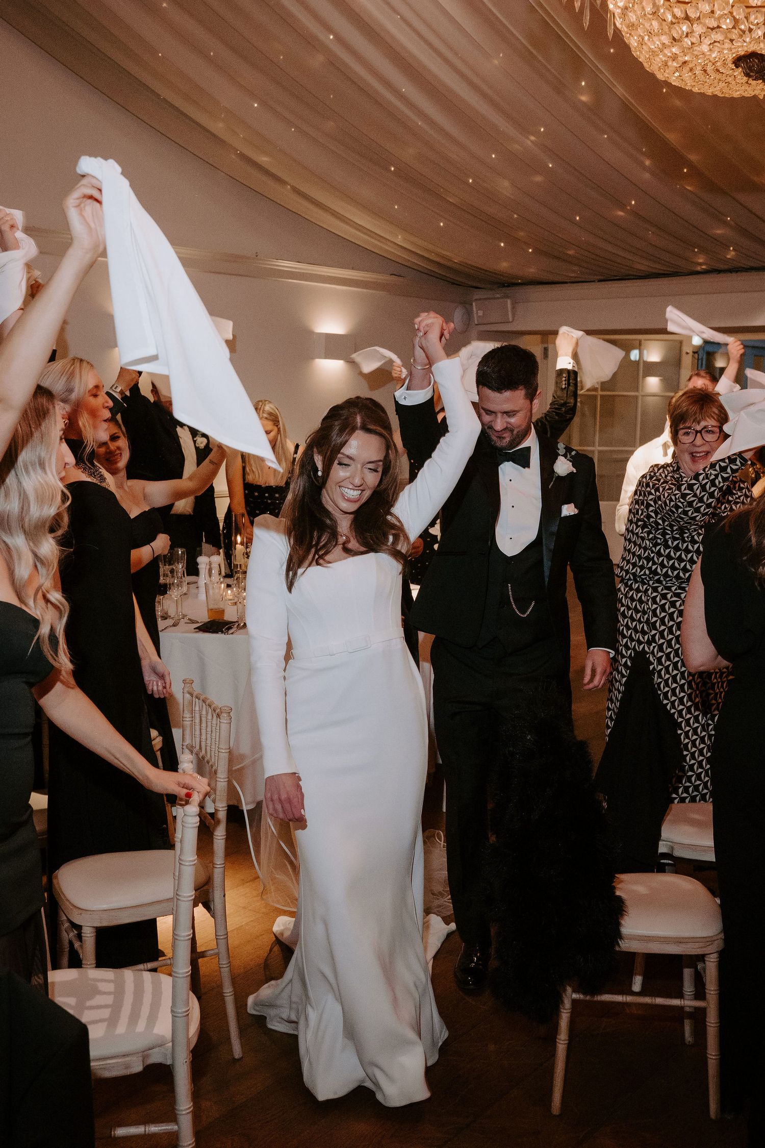 bride and groom entering wedding breakfast surrounded by guests cheering and waving napkins at Iscoyd park