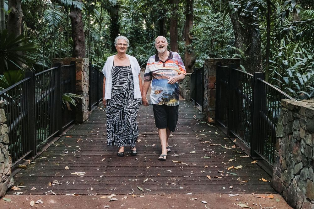 People walking along a wooden boardwalk path surrounded by lush tropical foliage in a rainforest setting.