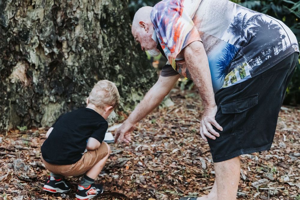 Two people explore and interact with fallen leaves on the ground in an outdoor natural setting.