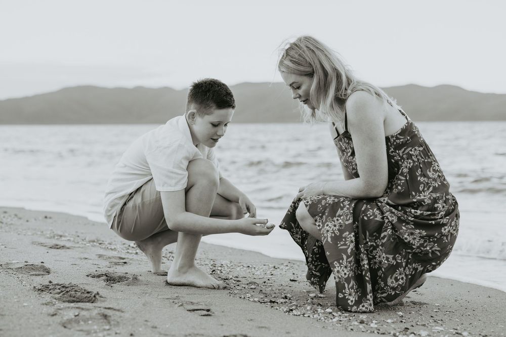 A series of black and white beach photos showing people playing and exploring in the sand at the water's edge.