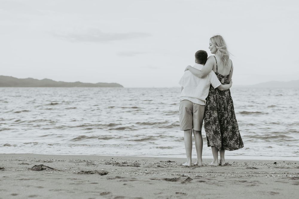Black and white photo of a couple walking along a scenic beach shoreline.