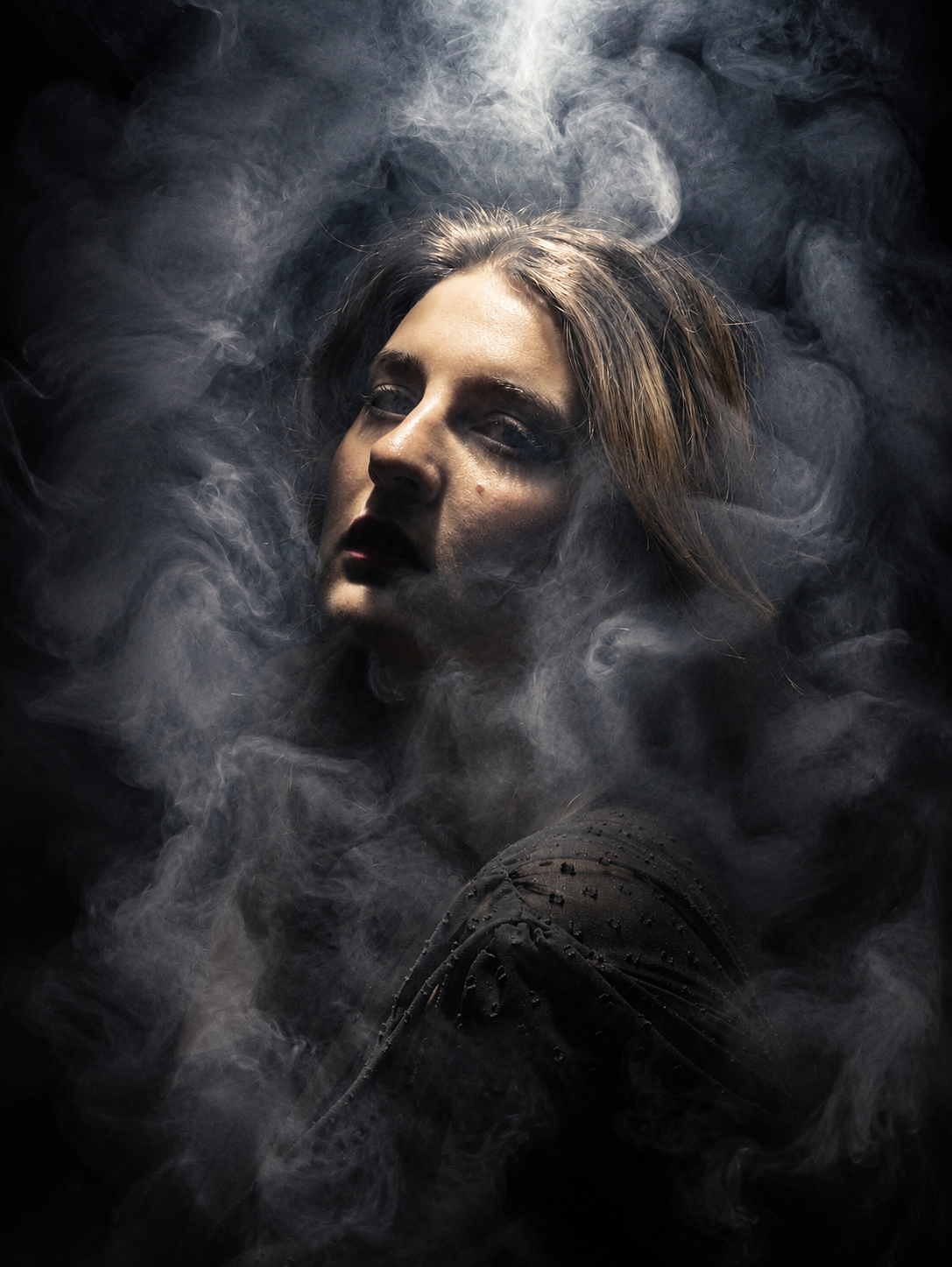 A mysterious woman surrounded by swirling smoke against a dark background, dramatic moody portrait photography.