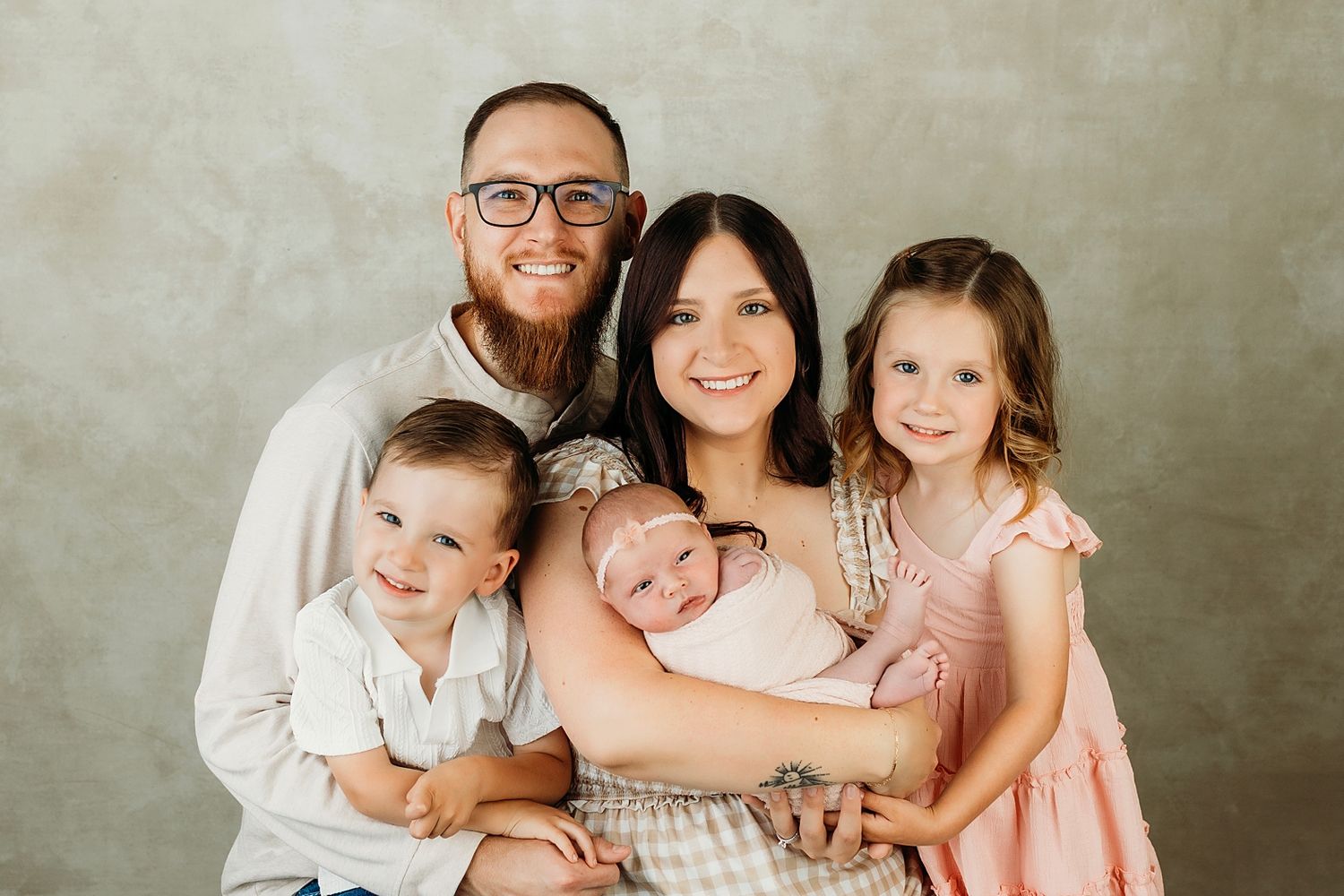 Happy family of five posing for a newborn portrait, parents with two toddlers and a sleeping baby in a studio.