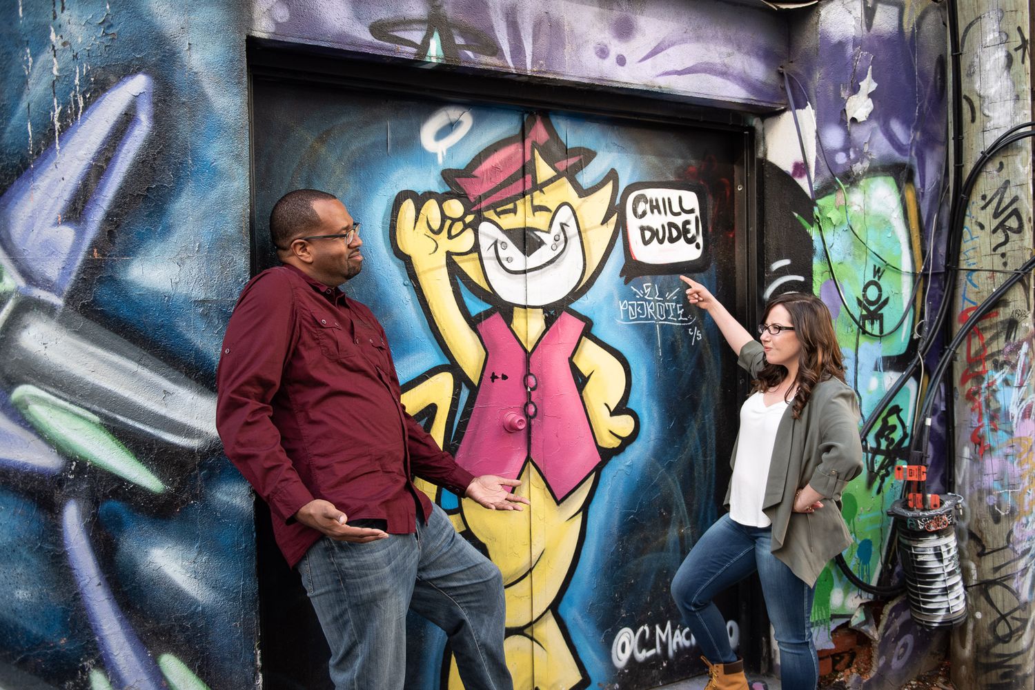 A couple laughs together while pointing at a cartoon tiger graffiti mural in a colorful urban alleyway in Graffity Alley in Toronto..