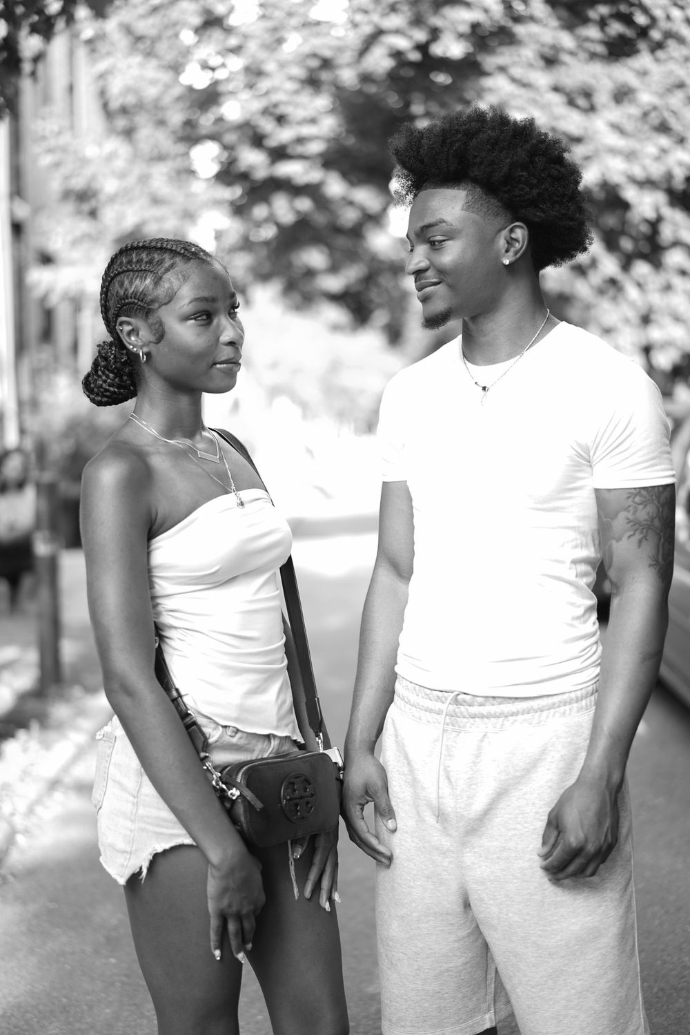 Black and white photo of a young couple holding hands and gazing at each other on a city street.