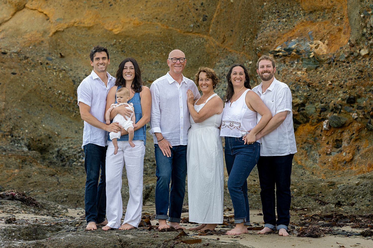 A multigenerational family of nine poses together smiling in a professional portrait, dressed in blue and white tones.