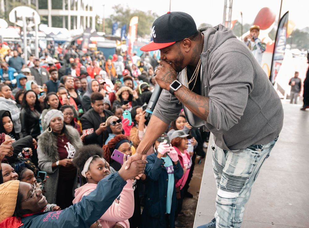 Rapper performs on stage leaning toward crowd of fans at an outdoor music event.
