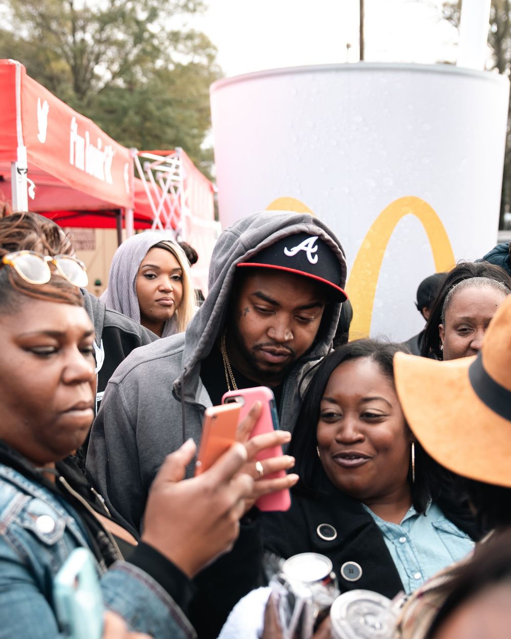 Crowd gathers around a man in Atlanta Braves cap near McDonald's booth at outdoor event.