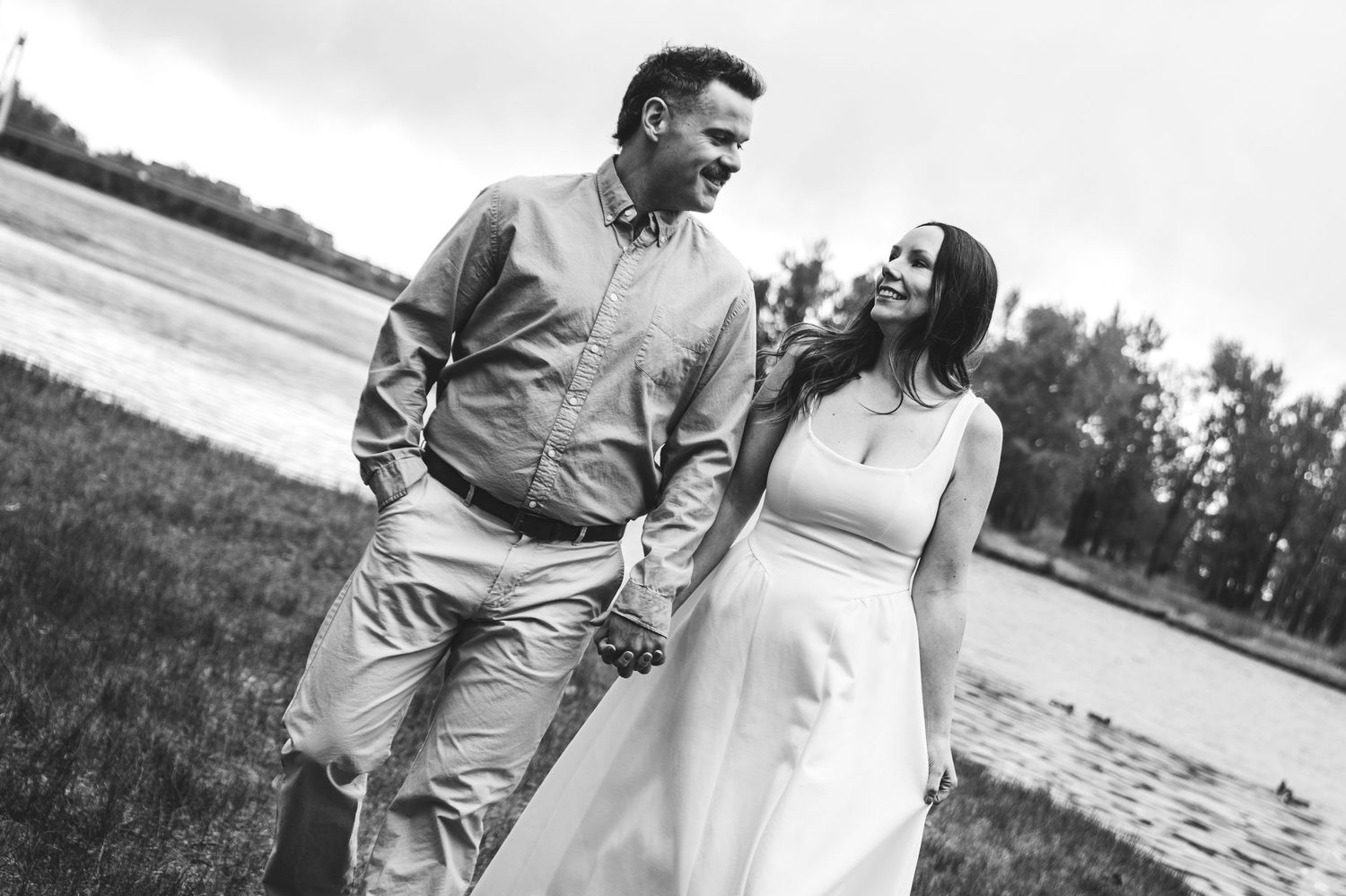 Couple holding hands on a lush green hill with mountains and cloudy sky in the background during engagement shoot.
