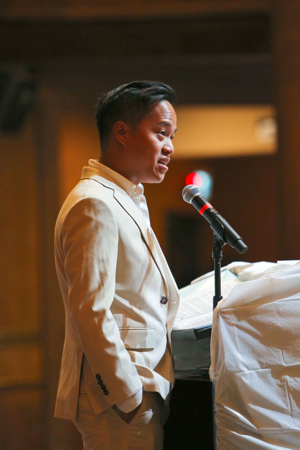 Young man in white blazer speaking at a podium with a microphone at a formal event.