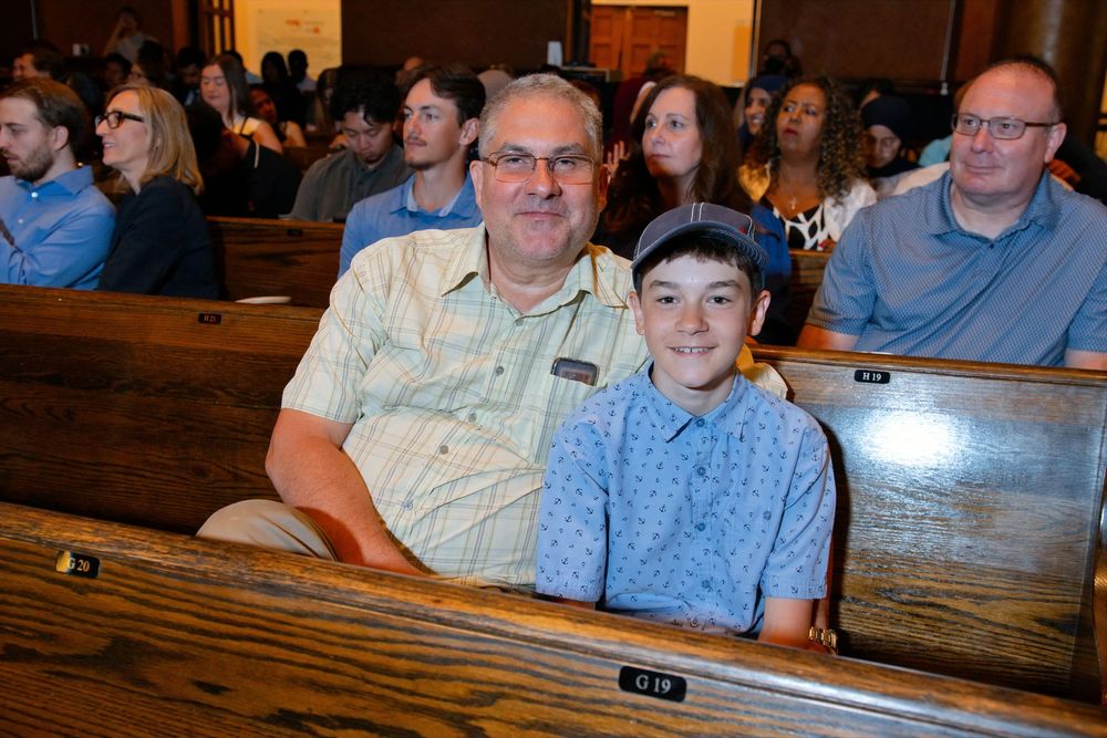 Man and young boy smiling together in church pews during a ceremony.