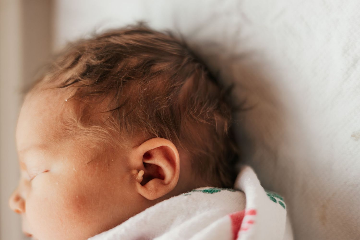 Close-up of a sleeping newborn baby with dark hair, resting peacefully on a white blanket | What's Labor Like for Fathers