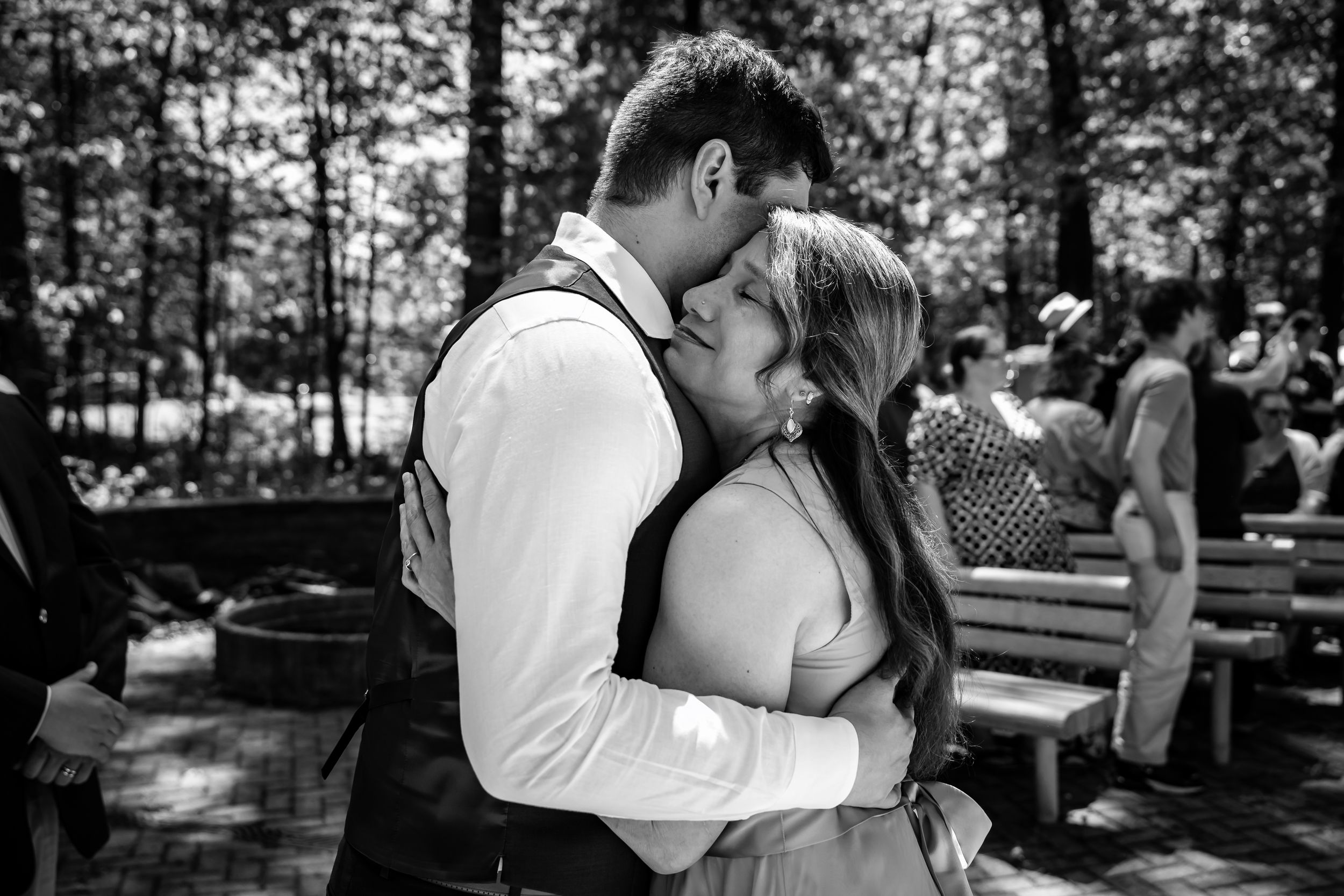 Black and white photo of newlywed couple sharing first kiss embrace at outdoor woodland wedding ceremony.