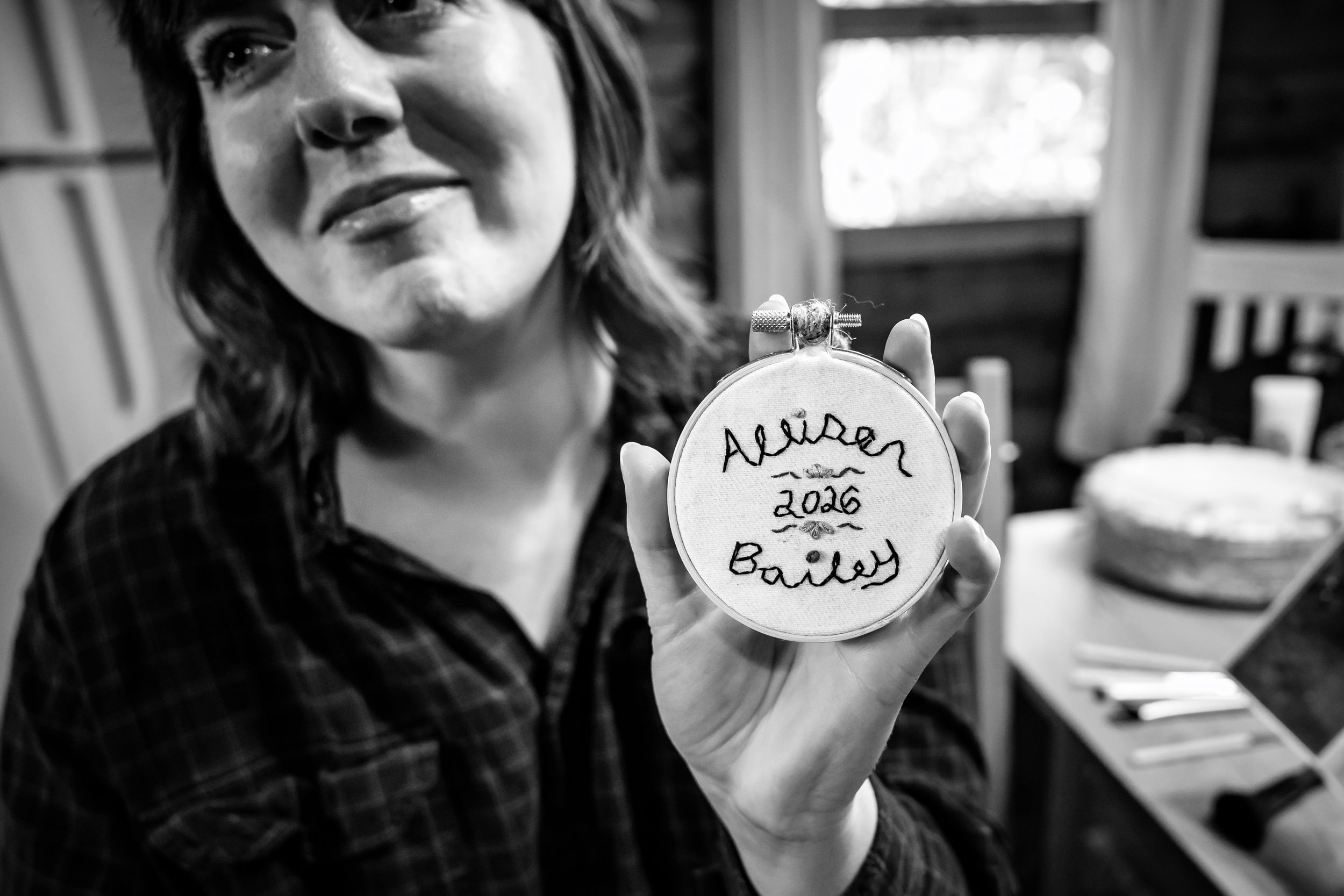 Woman holding embroidery hoop with hand-stitched text in black and white photo.