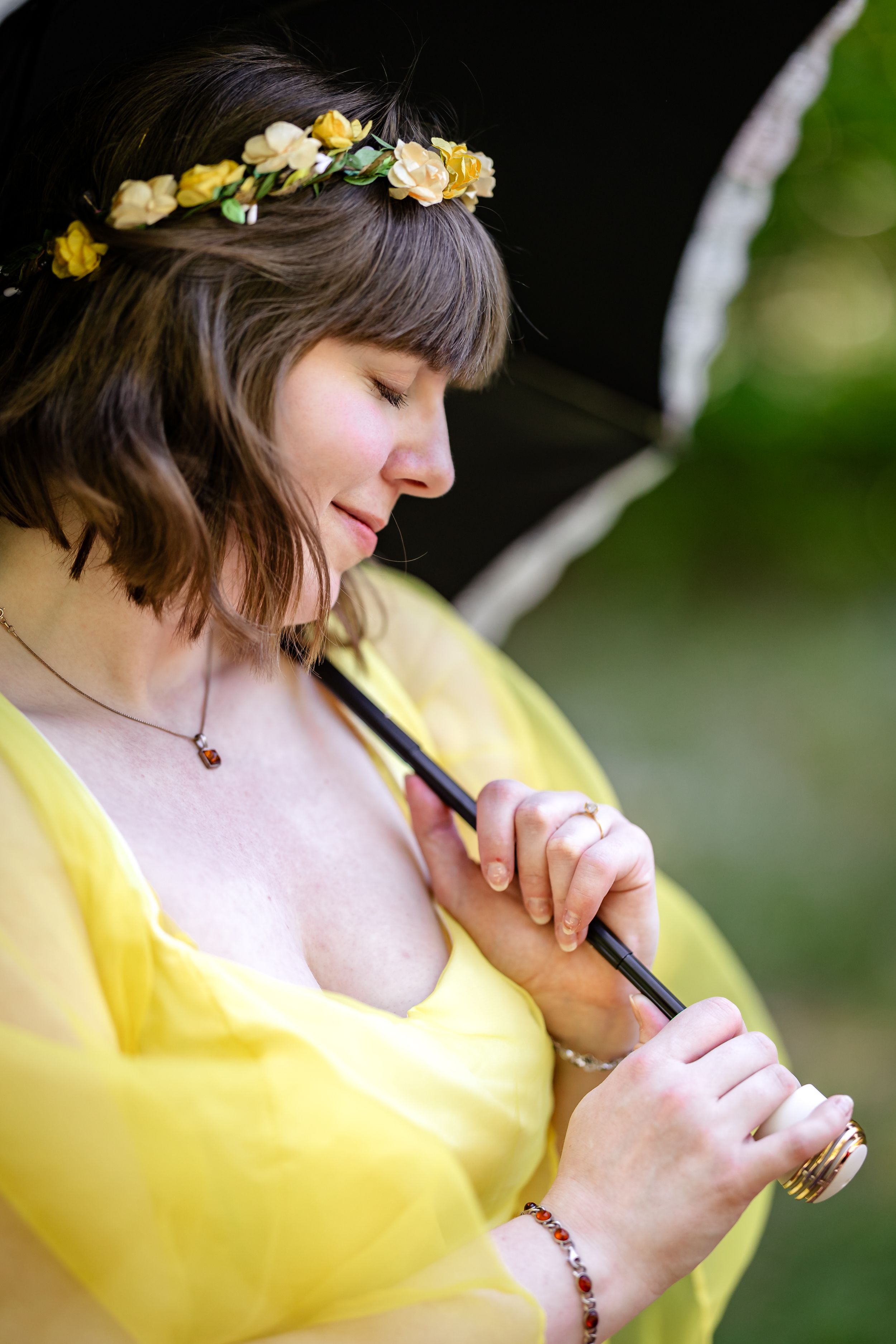 Close-up of bride in yellow dress wearing floral crown holding black umbrella outdoors.