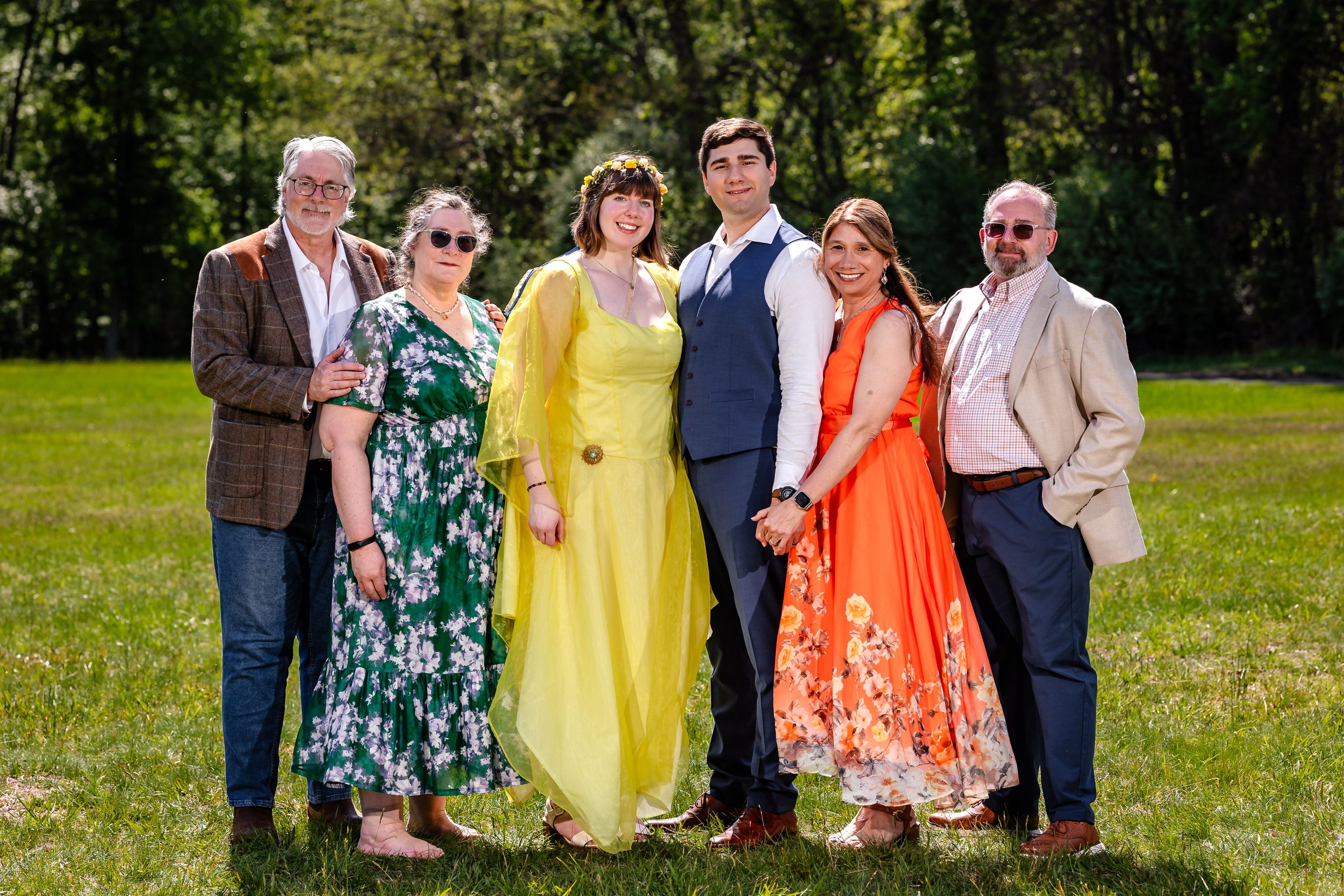 Wedding party of six posing together on green lawn in colorful formal attire.