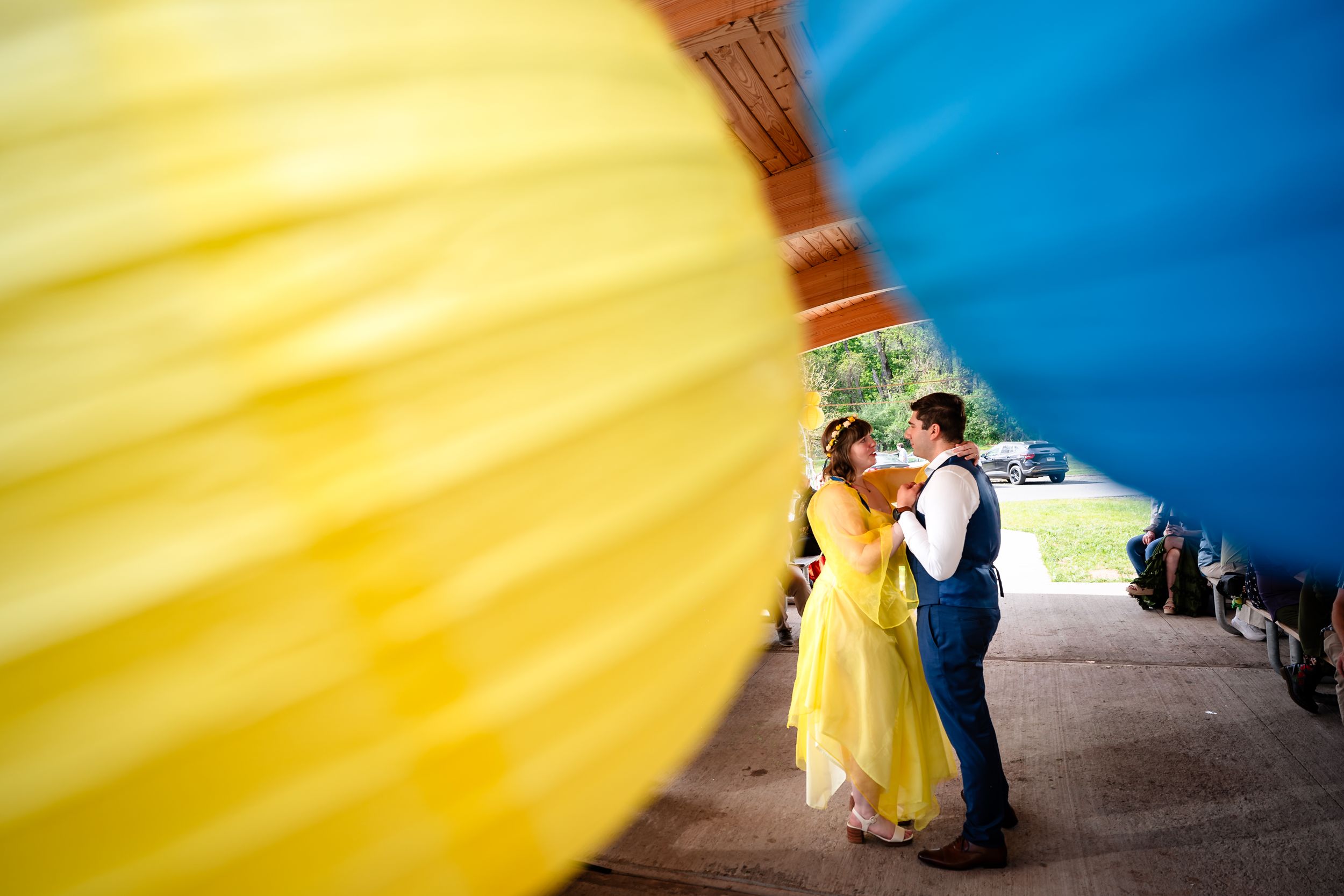 Bride in yellow gown and groom share a romantic moment framed by colorful hot air balloons.