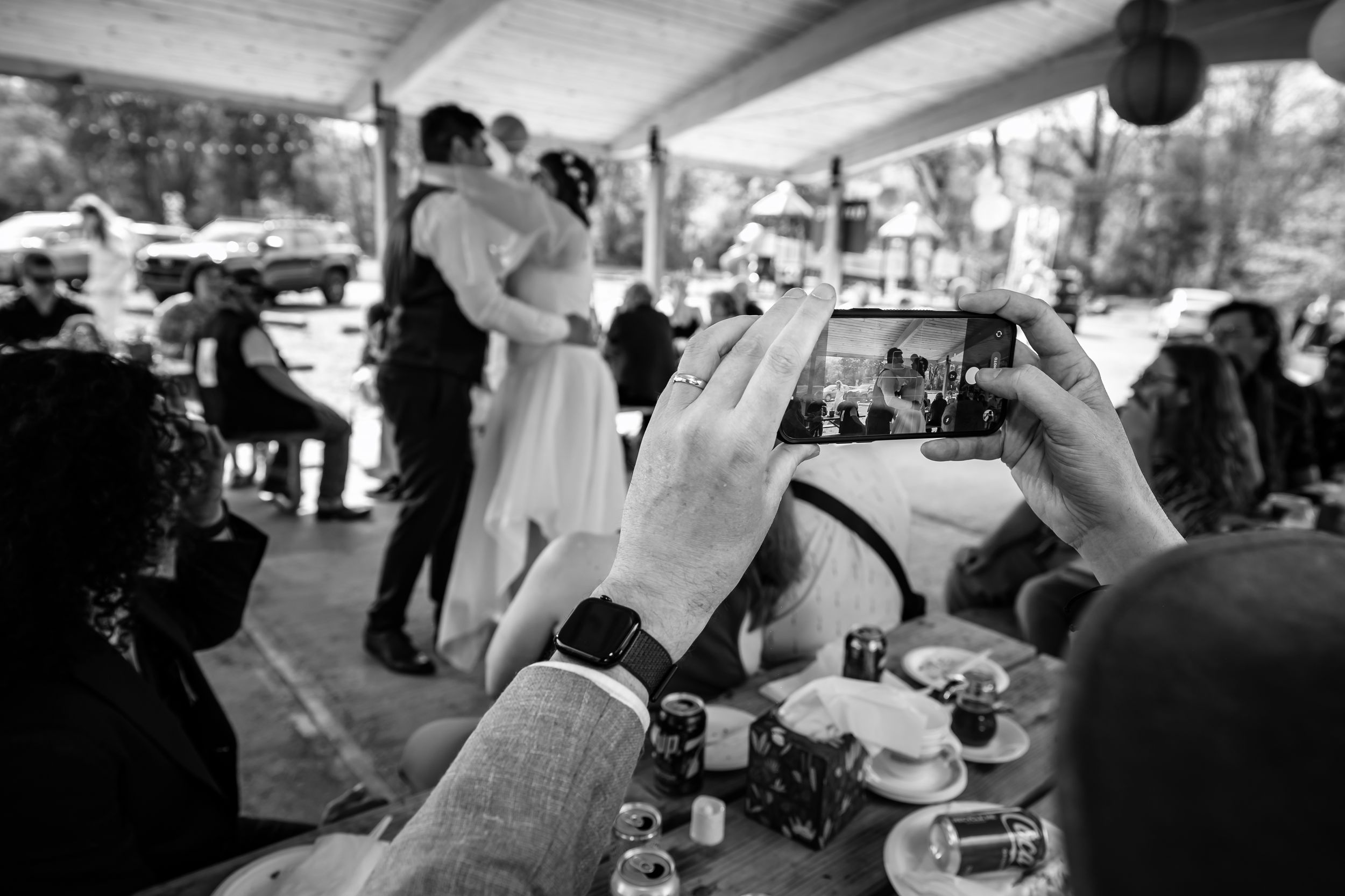 Guest photographs newlyweds dancing at outdoor wedding reception in black and white.