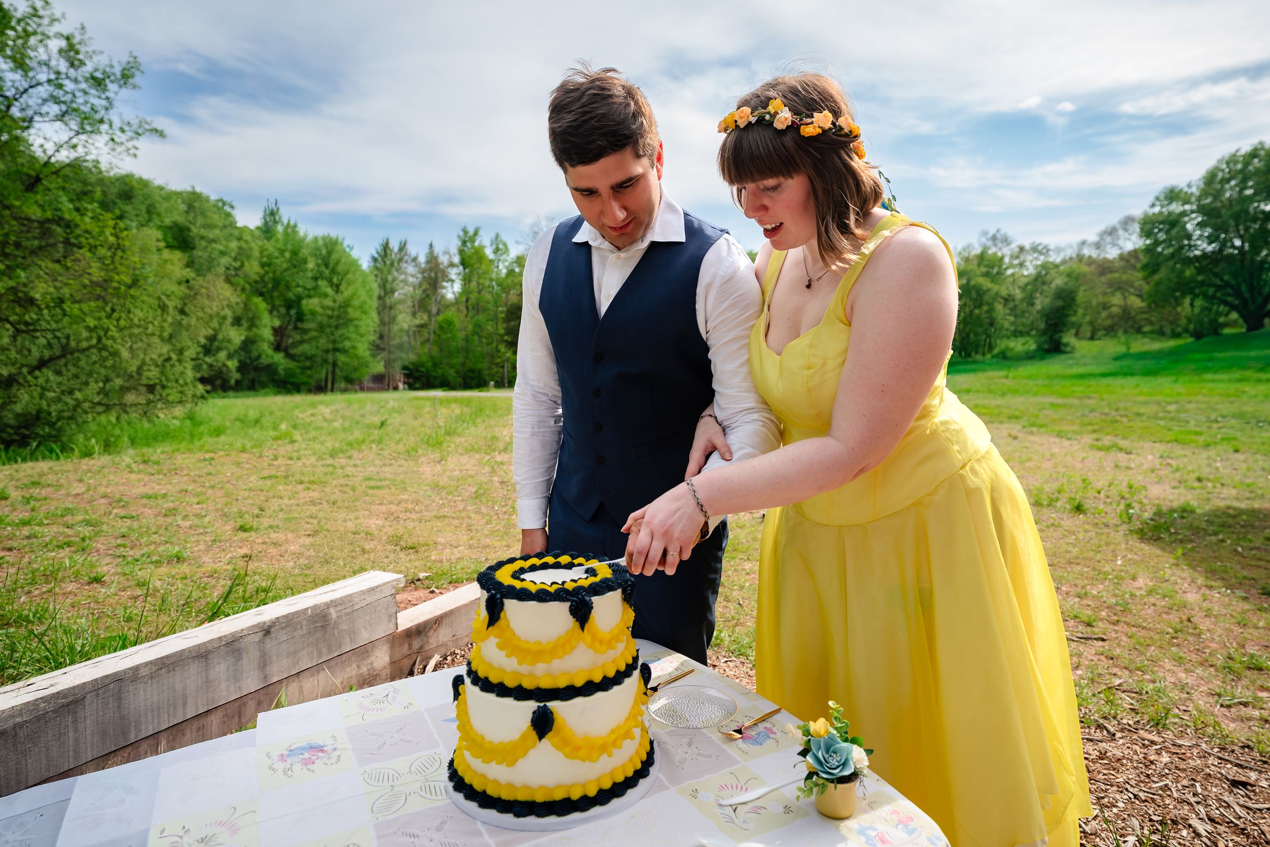 Bride in yellow dress and groom cutting a black and yellow wedding cake outdoors.