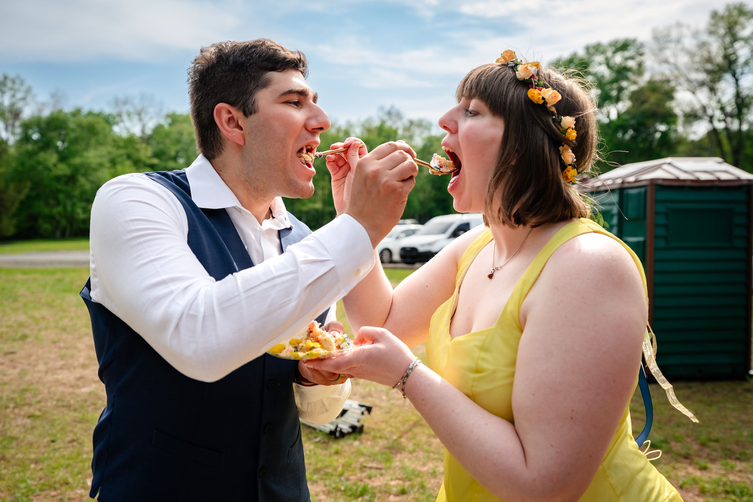 Bride and groom feeding each other cake at outdoor wedding celebration.