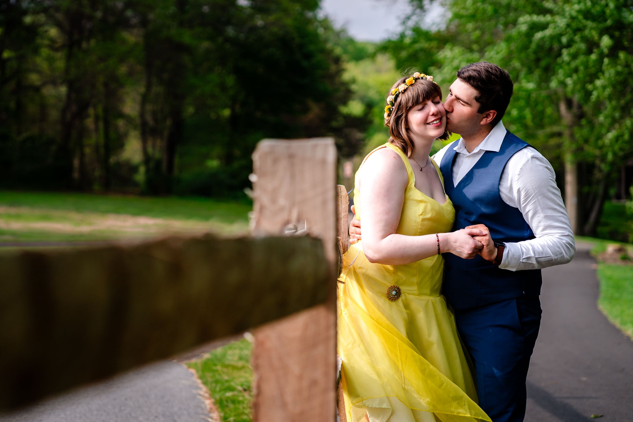 Bride in yellow dress and groom sharing a romantic kiss in a park.