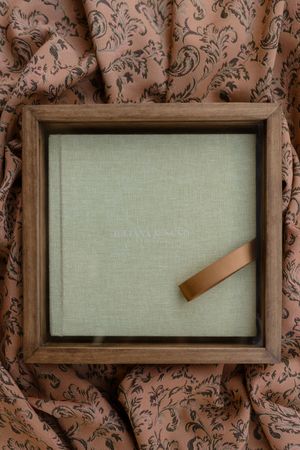 A series of wooden frames showing the progressive assembly of a linen-covered photo album against a patterned wallpaper.